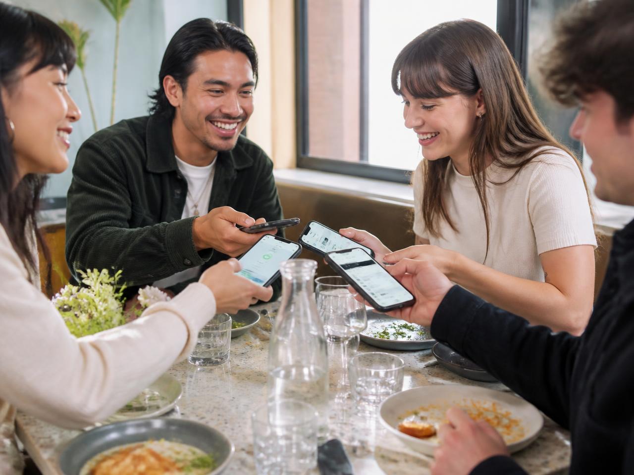 Friends splitting the bill from their phones at a restaurant table